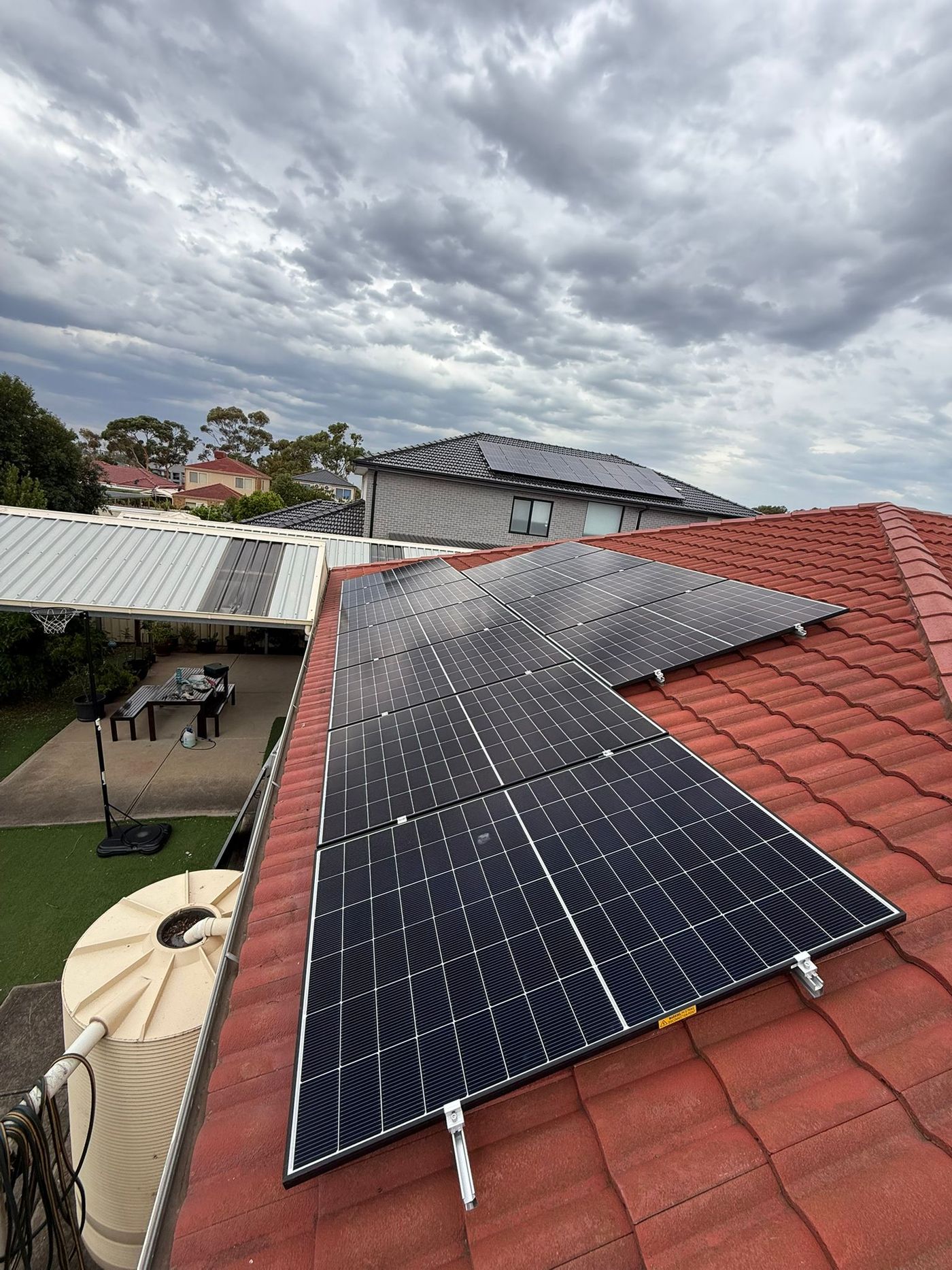 L-shaped solar array on a tiled roof under storm clouds